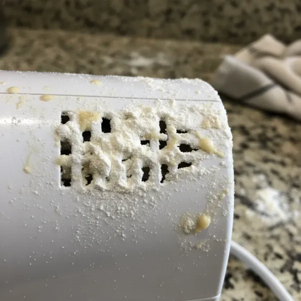 Hand mixer with clogged vents from flour dust, highlighting maintenance need.