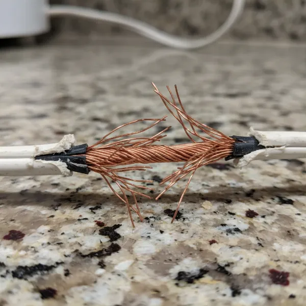 Close-up of a damaged hand mixer cord with exposed wires, illustrating electrical hazards.